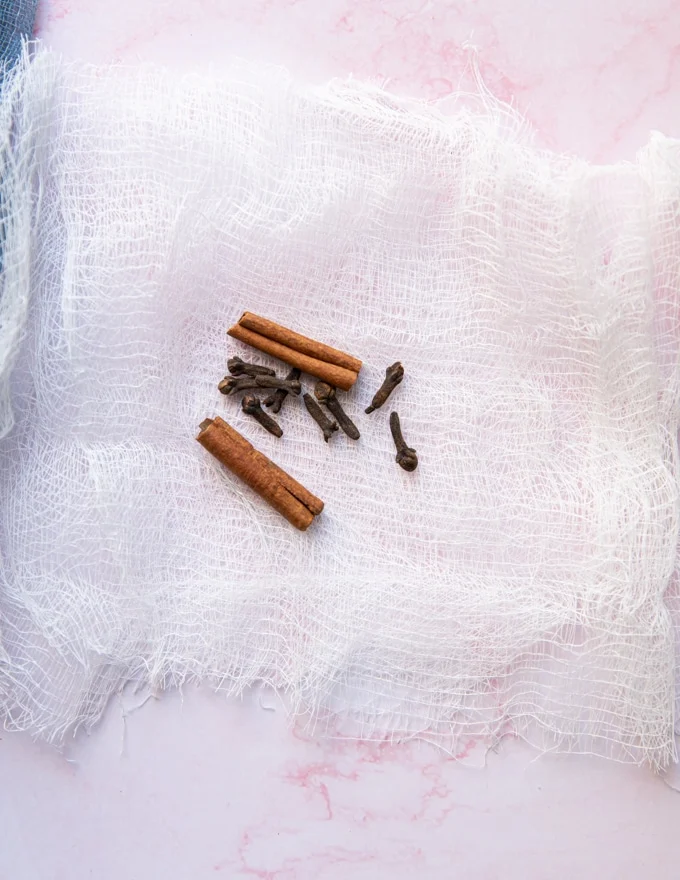 A stick of cinnamon and 6 whole cloves over a cheesecloth ready to tie up to flavor the jam