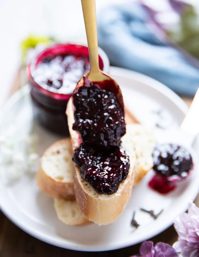 A spoon spreading some homemade blackberry jam recipe over the baguette to serve showing the consistency and final texture of the homemade jam