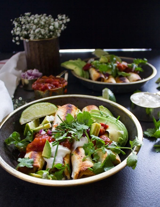 a plate of chicken flautas cooked and ready, topped with salsa, avocado, sour cream and lots of cilantro