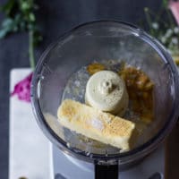 A bowl in a food processor with the cooked garlic, the butter and seasoning