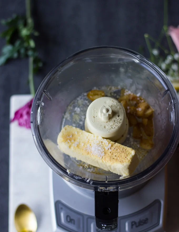 A bowl in a food processor with the cooked garlic, the butter and seasoning