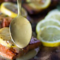 sockeye salmon on a plate and a hand drizzling the lemon butter sauce over the cooked sockeye salmon recipe