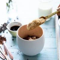 A spoon adding in the brown sugar to the mug to make brownie in a mug