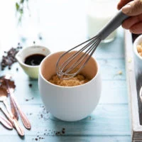 A hand holding a small whisk to whisk in the dry ingredients in the mug to make brownies