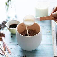 A spoonful of milk added to the mug to make the brownie in a mug batter
