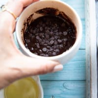 A hand holding a brownie in a mug ready to go in the micowave