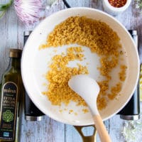 A spatula tossing the bread crumbs in a skillet until toasty and ready