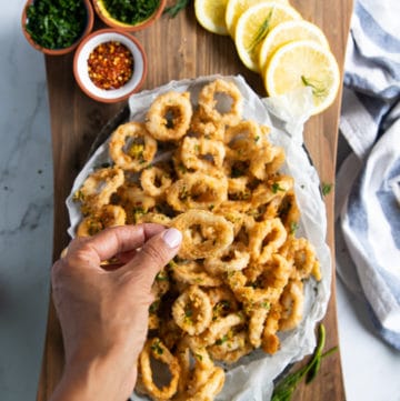 A hand holding a piece of calamari over a plate of fried calamari showing the crispy texture