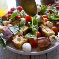 A spoon drizzling the delicious caprese salad dressing over caprese salad recipe