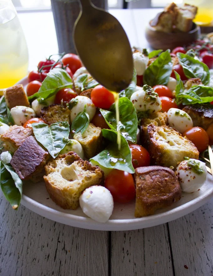 A spoon drizzling the delicious caprese salad dressing over caprese salad recipe