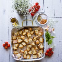 some stale bread chunks on an oven dish surrounded by garlic, olive oil, oregano and chilli flakes to make homemade croutons