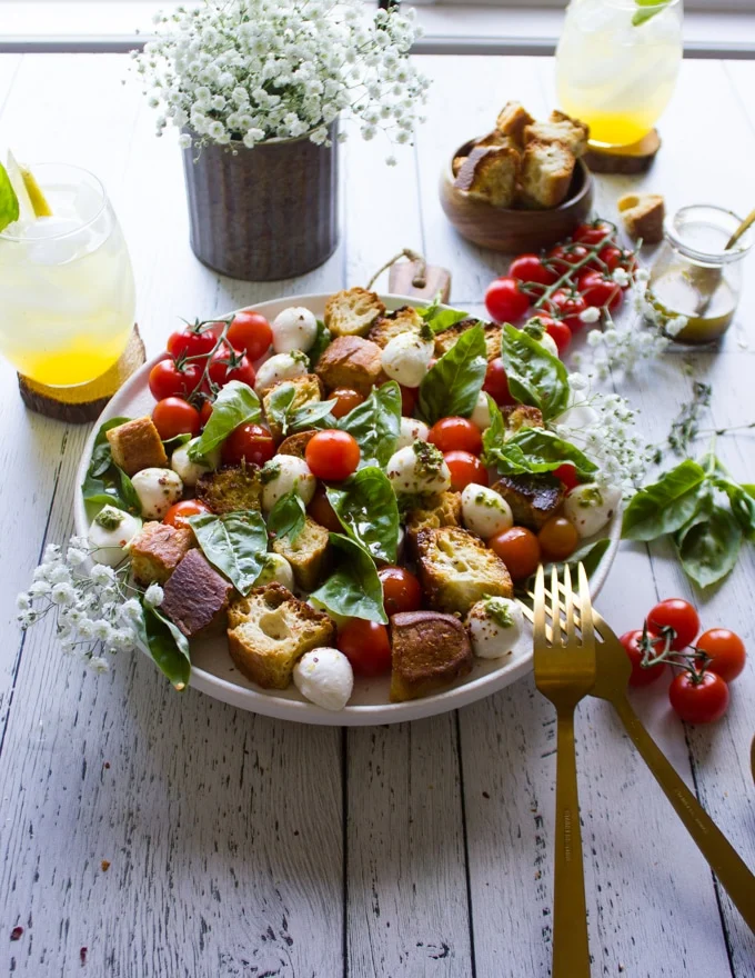 two forks on a plate of caparese salad surrounded by lots of fresh basil