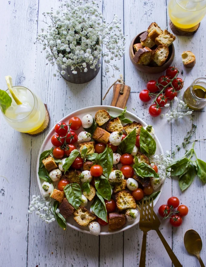 The caprese salad ready on a plate with extra croutons on the side and extra salad dressing.