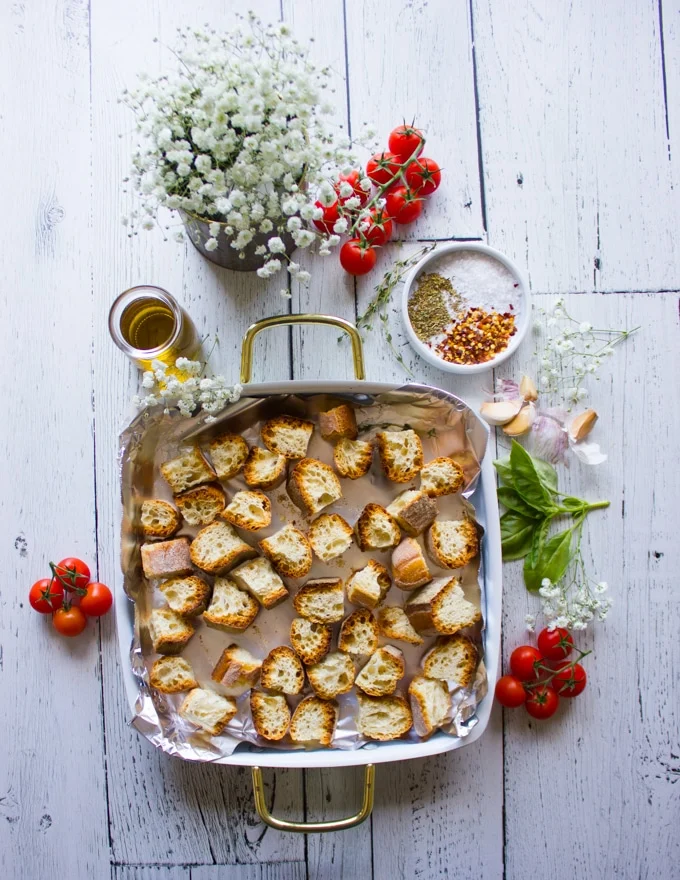 some stale bread chunks on an oven dish surrounded by garlic, olive oil, oregano and chilli flakes to make homemade croutons
