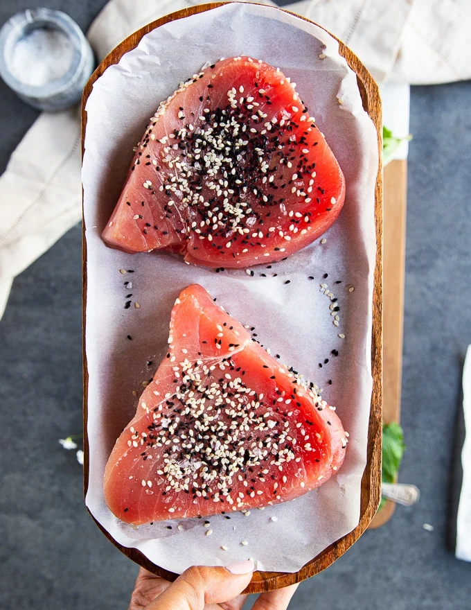seasoned tuna steaks with sesame seeds and salt on a parchment paper ready to sear