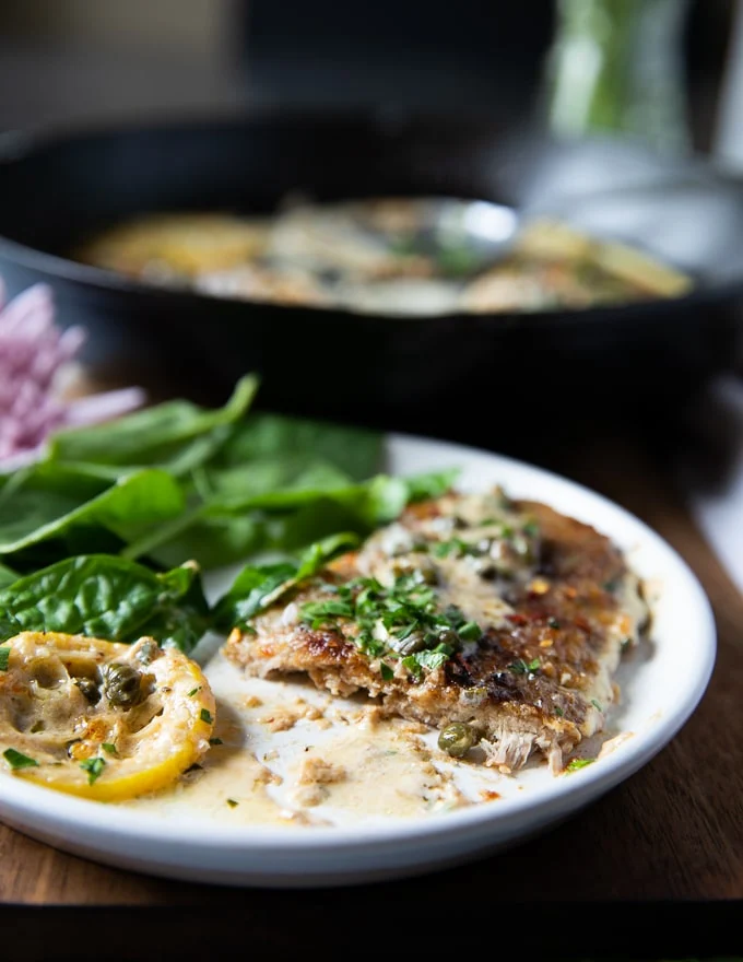 A piece of veal scallopini cur in half on a plate showing the inside of it served with spinach salad