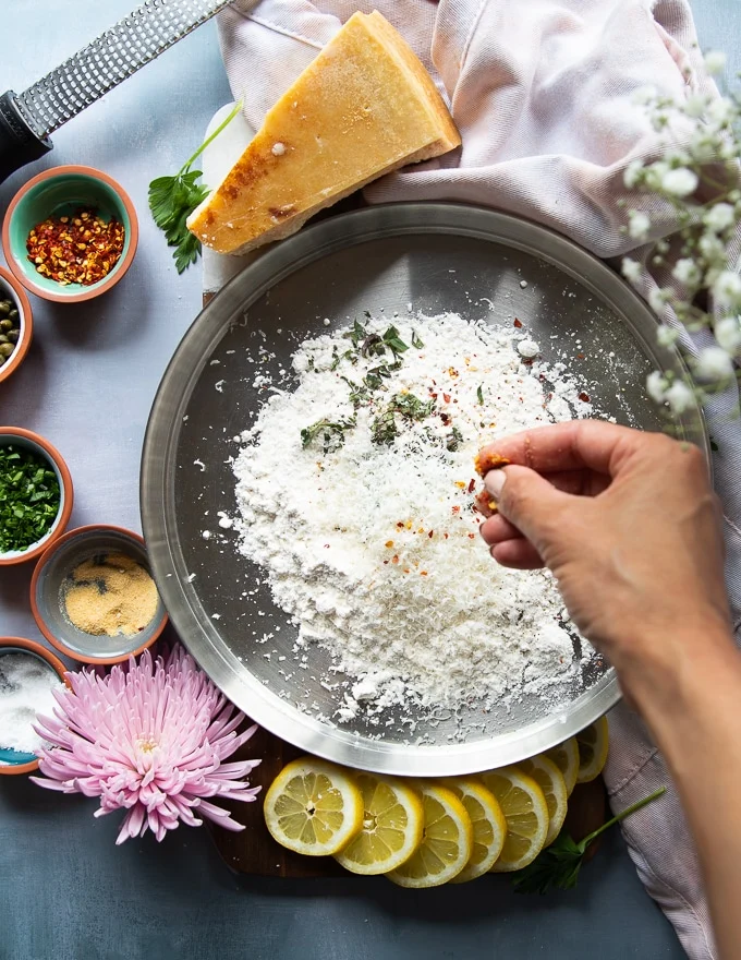 A hand sprinkling some spice on the flour bowl to coat the veal before searing