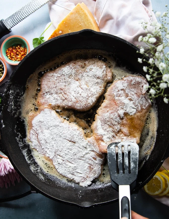 The veal scallopini placed in a large cast iron pan with melted butter