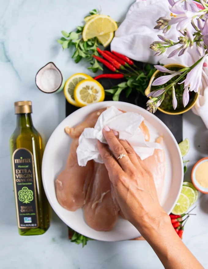 a hand patting down the chicken breasts before seasoning