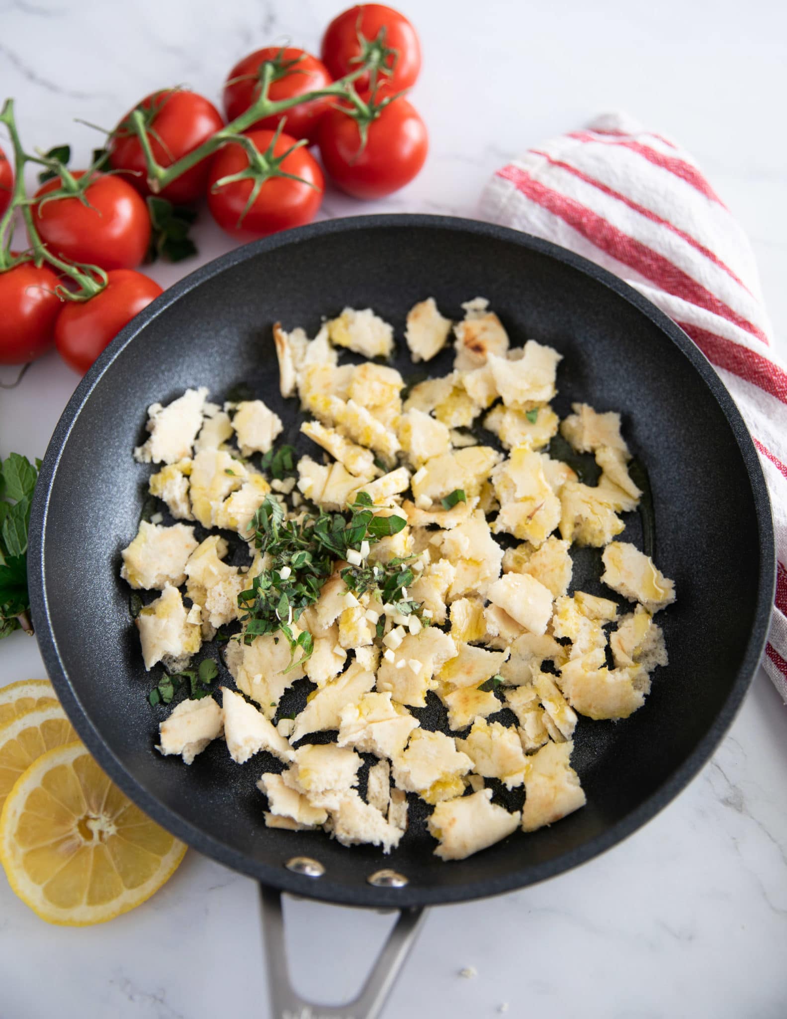 torn up pita chunks in a skillet and osme oregano on top, and fresh garlic and olive oil , ready to be tossed