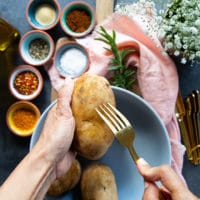 A hand holding a Russet Potato and pricking it with a fork