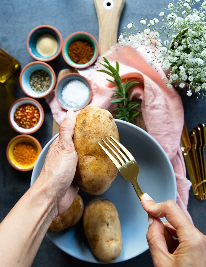A hand holding a Russet Potato and pricking it with a fork
