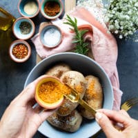 Russet Potatoes in a bowl and a hand sprinkling some seasoning over the potatoes