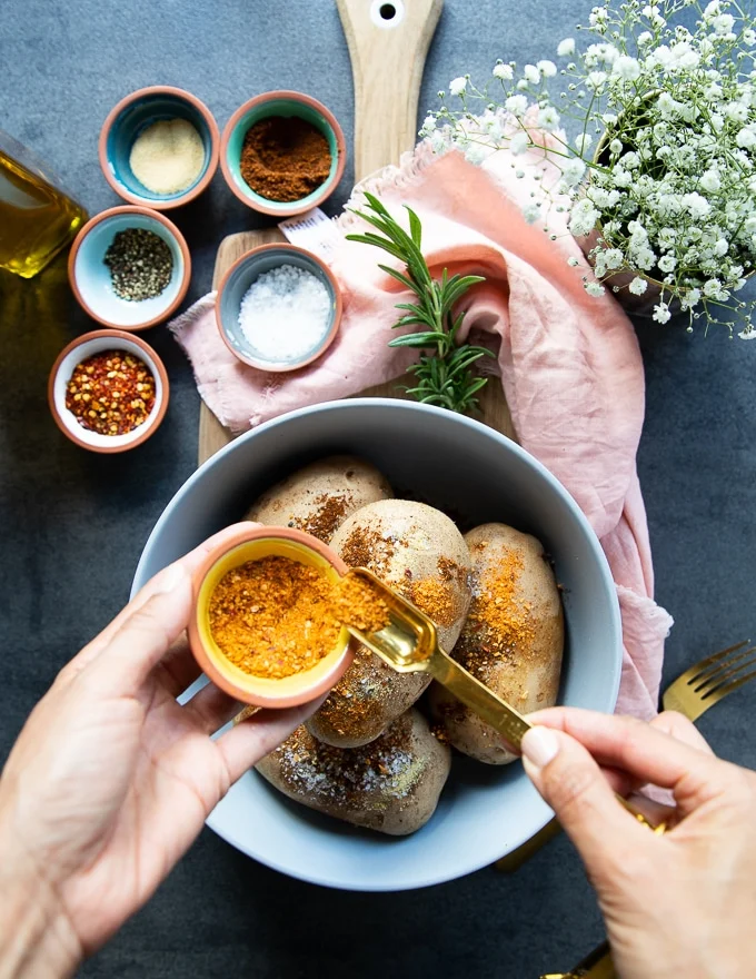 Russet Potatoes in a bowl and a hand sprinkling some seasoning over the potatoes