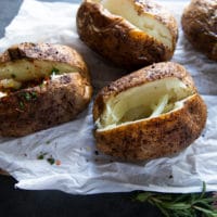 Air fried baked potatoes placed in a paper on a board and sliced in half