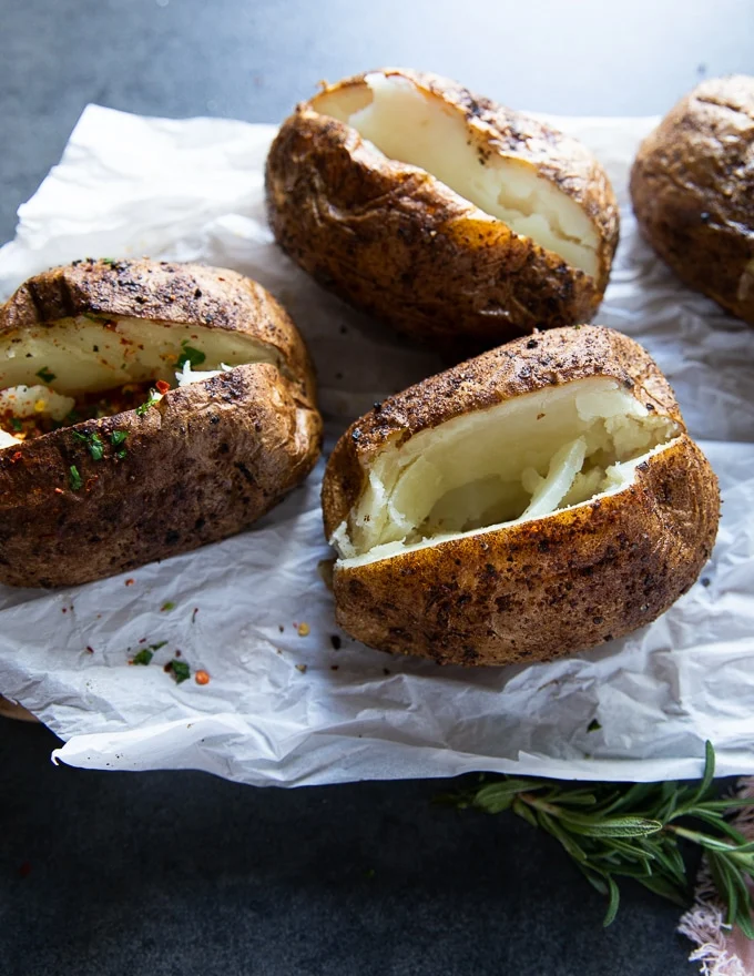Air fried baked potatoes placed in a paper on a board and sliced in half