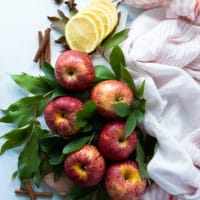 A board filled with Gala apples surrounde dby apple leaves and lemon slices and cinnamon sticks