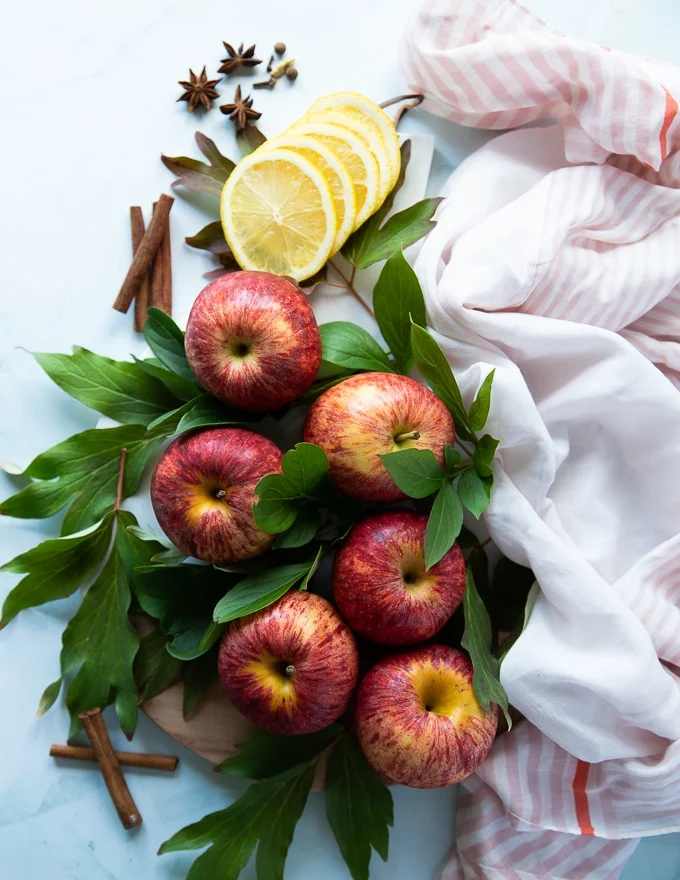 A board filled with Gala apples surrounde dby apple leaves and lemon slices and cinnamon sticks