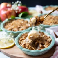 A spoon holding a piece of apple crumble and vanilla ice cream showing the saucy inside of the crumble