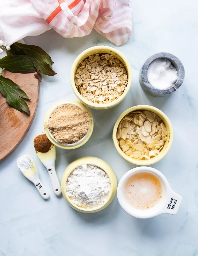 small bowls with ingredients for the apple crumble topping including butter , flour , sugar , oats , cinnamon and spices