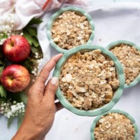a hand holding the apple dessert topped with the crumble topping and ready to bake