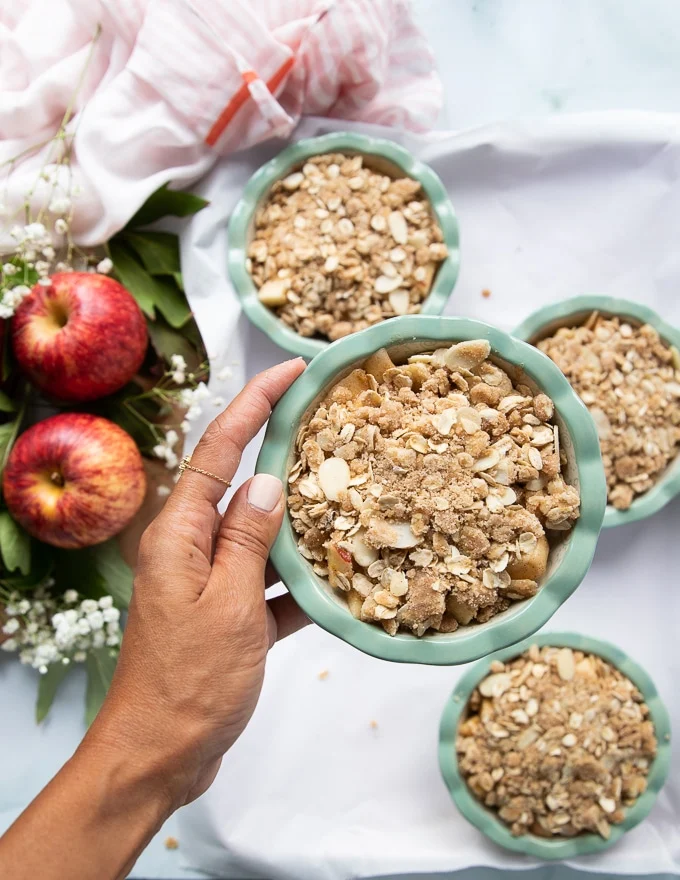 a hand holding the apple dessert topped with the crumble topping and ready to bake