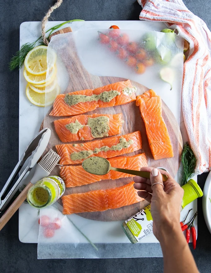 A hand drizzling the grilled salmon marinade over pieces of salmon fillets on a white marble