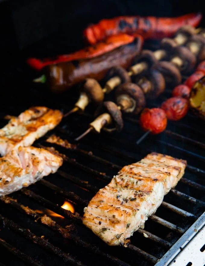 flipped salmon over the bbq grill showing the texture and chars o the salmon, also grilled veggies on the BBQ next to the salmon