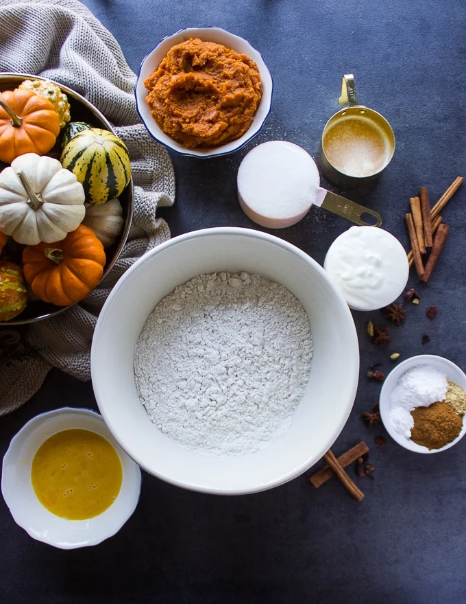 ingredients to make pumpkin donuts including flour, pumpkin, eggs, yogurt, oil, sugar, cinnamon and melted butter