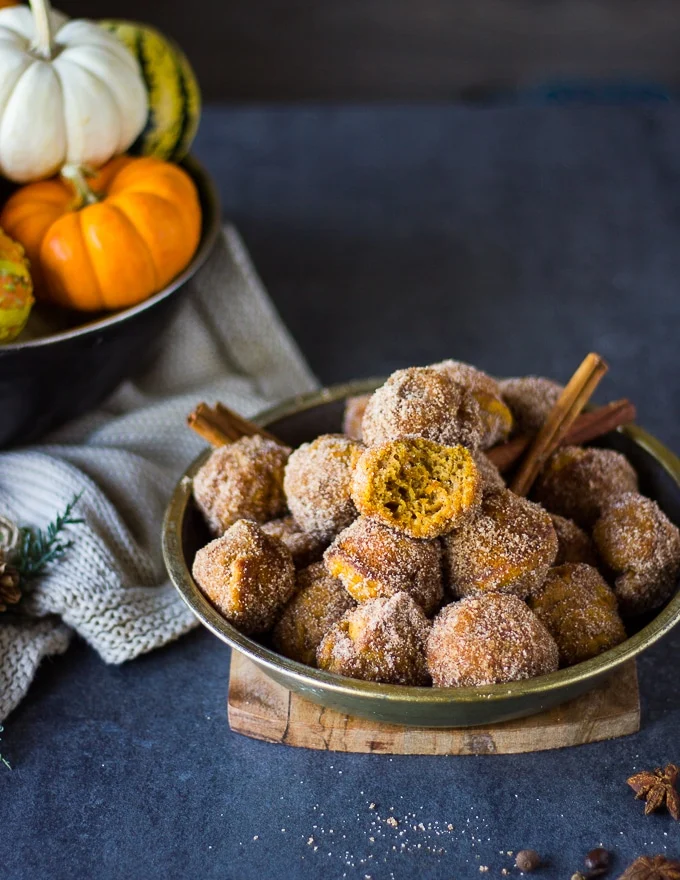 a plate with pumpkin donuts coated in cinnamon sugar in a bowl surrounded by pumpkins
