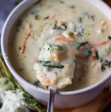 A bowl of chicken and gnocchi soup and a spoon scooping out some soup to show the texture