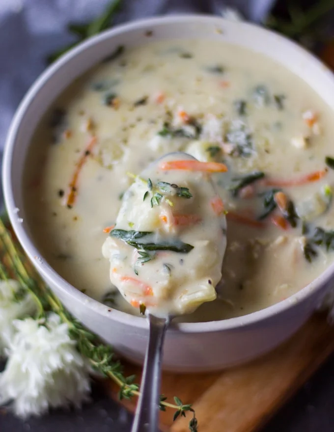 A bowl of chicken and gnocchi soup and a spoon scooping out some soup to show the texture