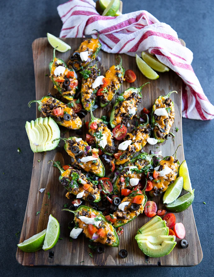 A whole board of jalapeno popper served with some nacho toppings like onions, sour cream, tomatoes and avocado