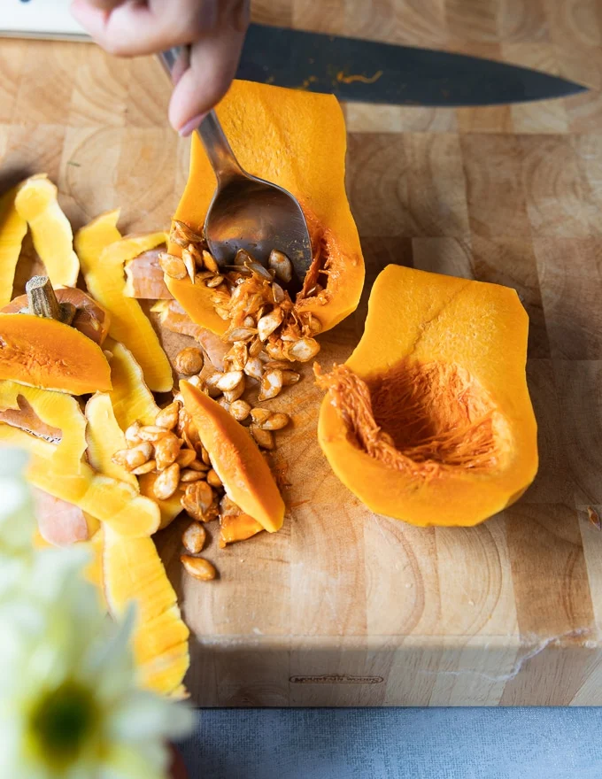 a spoon scooping out the seeds form inside the squash