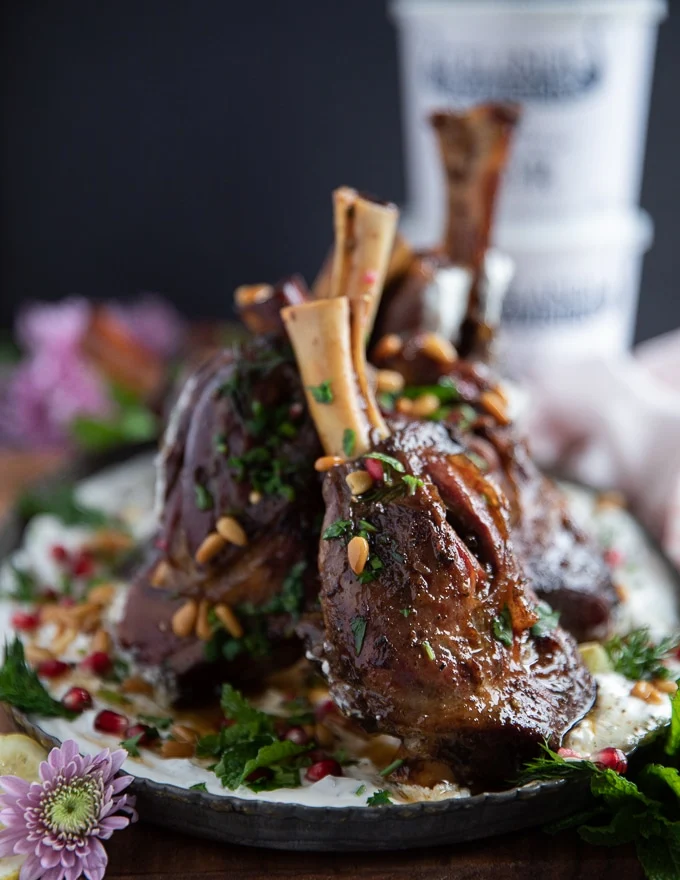 lamb shanks are placed over the skyr sauce and hen garnished with parsley, pine nuts and pomegranate arils