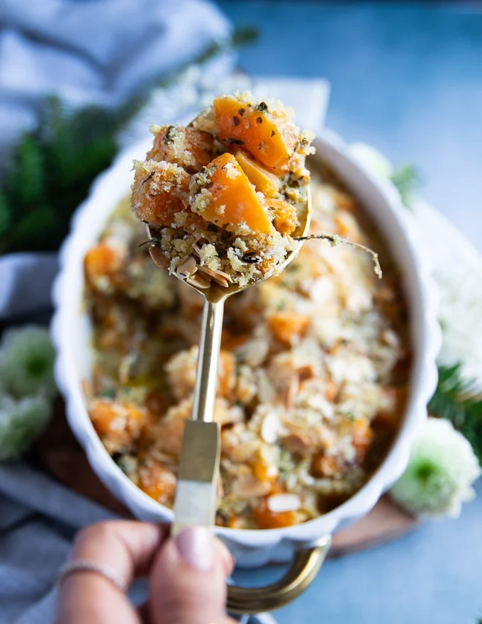 A hand holding up a generous serving of butternut squash casserole showing the texture of the casserole and the soft butternut squash