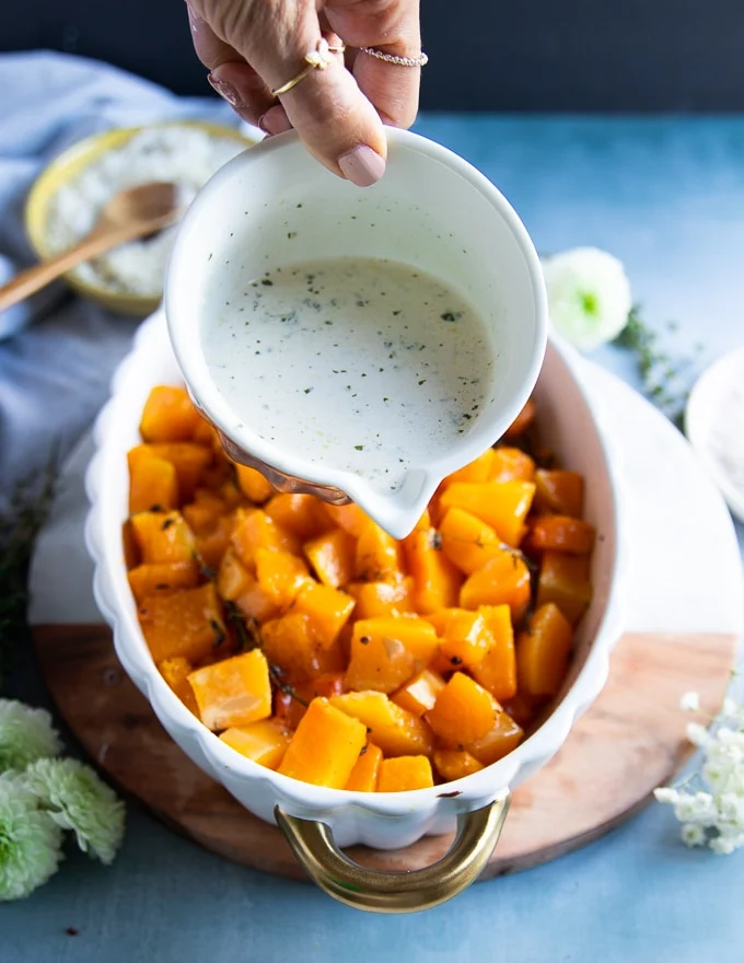 A hand drizzling the basil cream over the fully roasted butternut squash