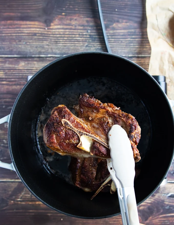 A hand holding one lamb shoulder chop showing the golden seared crust on the meat