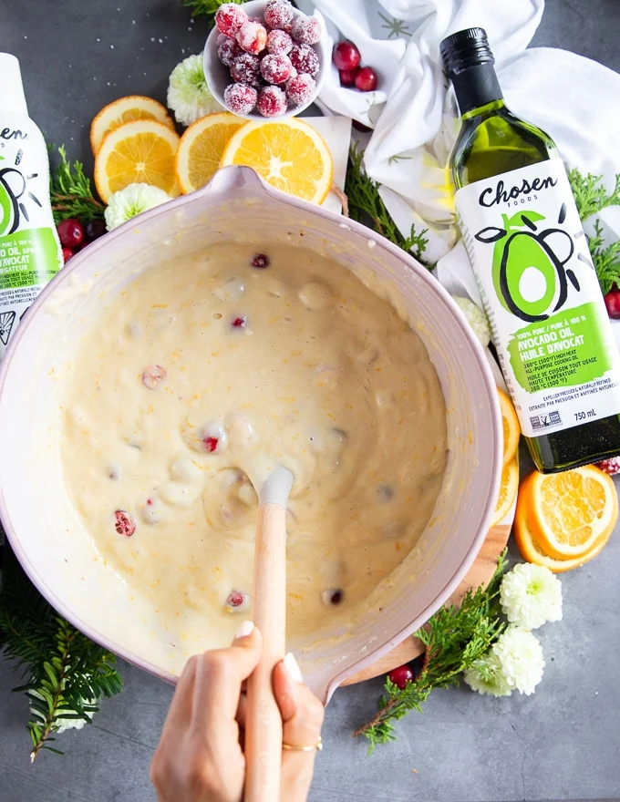 A hand holding a spatula mixing in the cranberries int the cake batter