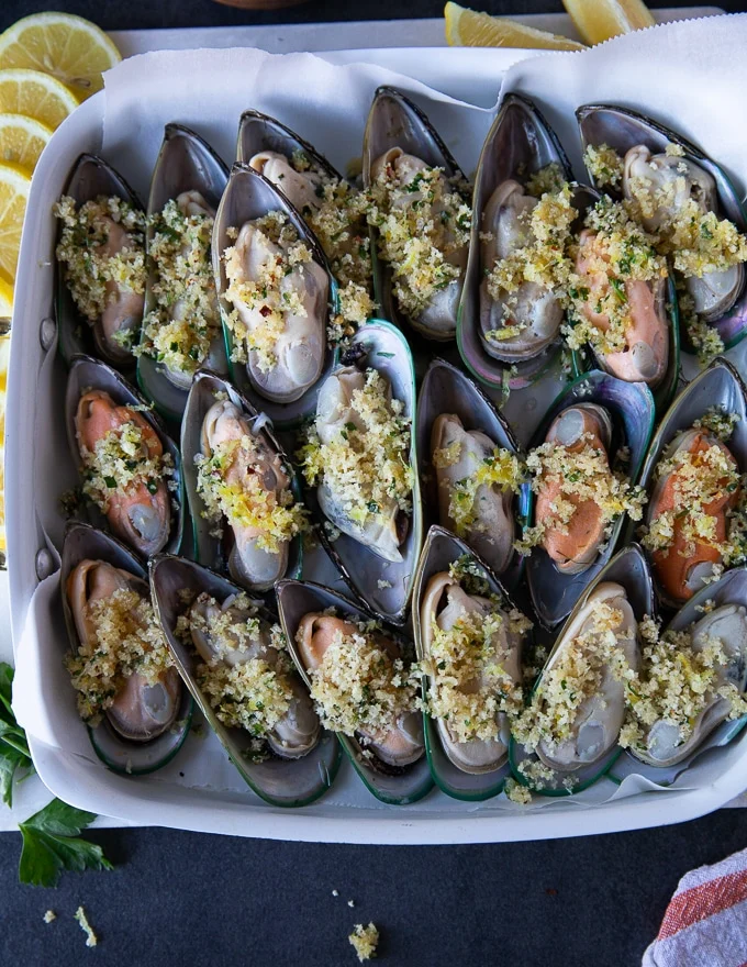 new zealand mussels or green mussels in a single layer on a baking sheet topped with the panko mixture and ready to go in the oven